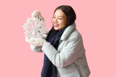 Pembe arka planda kar taneleri olan sıcak atkısı ve eldivenleri olan güzel Asyalı genç bir kadın.