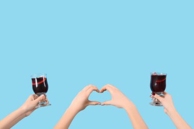 Mavi arka planda sıcak şarap kadehleriyle kadın elleri.