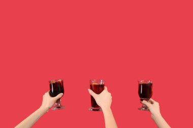 Kırmızı arka planda sıcak şarap kadehleriyle kadın elleri.