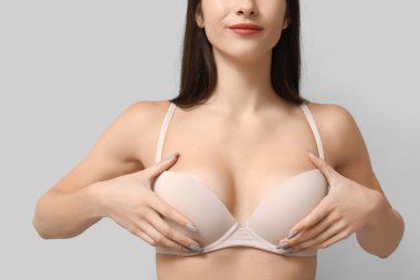 Gri arka planda göğüslerini kontrol eden genç bir kadın.