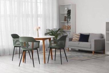 Masası, sandalyeleri, çiçekleri, kanepesi ve raf ünitesi olan rahat bir oturma odası.