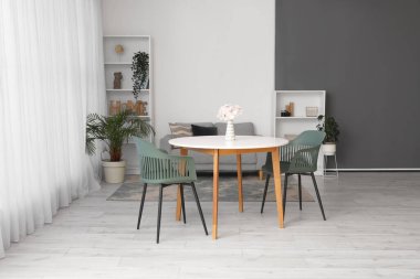 Masası, sandalyeleri, kanepesi, çiçekleri ve raf ünitesi olan geniş bir oturma odası.