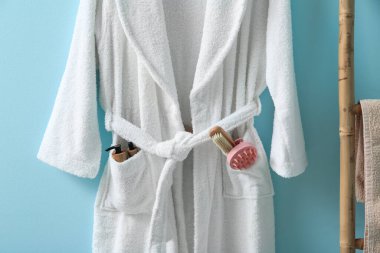 Mavi arka planda farklı banyo malzemeleri asılı beyaz bornoz.