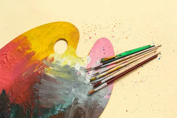Sanatçı fırçaları ve bej arka planda boya paleti