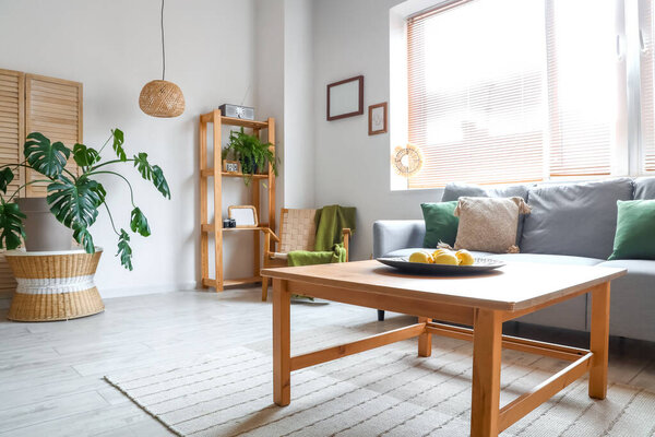 Cozy grey sofa and plate with lemons on wooden coffee table in interior of living room
