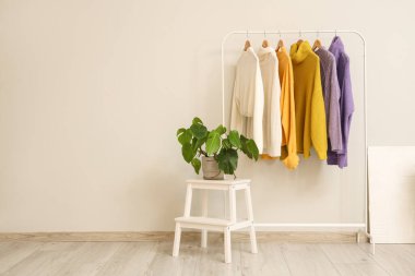 Beyaz duvarın yanında şık kıyafetler ve bitkiler var.