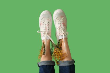 Yeşil arka planda mimoza çiçekleri olan spor ayakkabılı güzel genç bayanların bacakları.