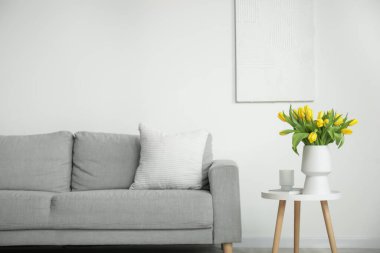 Oturma odasındaki gri kanepenin yanındaki sehpada duran sarı lalelerin güzel vazosu.