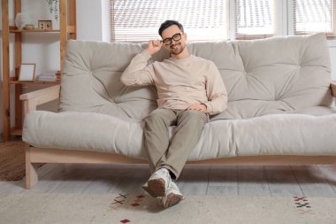 Evdeki kanepede oturan gözlüklü yakışıklı genç adam.