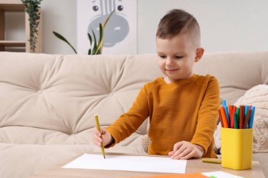 Evdeki masada keçeli kalemlerle çizen sevimli küçük çocuk.