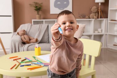 Evde keçeli kalem çizimi yapan sevimli küçük çocuk.