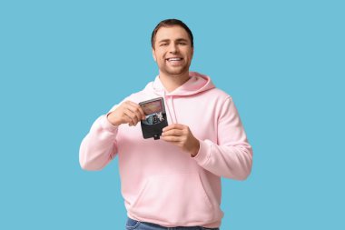 Mavi arka planda hediye kartı olan cüzdanı tutan genç bir adam.