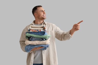 Giysileri olan genç adam arka plandaki bir şeyi işaret ediyor.