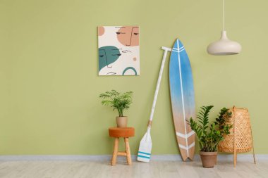 İçinde tahta sörf tahtası, bitki ve yeşil duvarın yanındaki resim olan ışık odasının içi.
