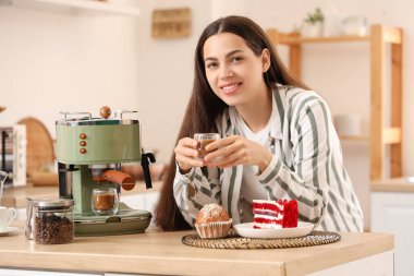 Modern kahve makinesi ve mutfaktaki tatlılarla güzel, genç ve mutlu bir kadın.