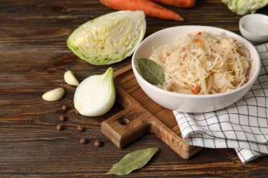 Lezzetli lahana turşusu kasede ve ahşap arka planda malzemeler