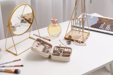 Pencerenin yanındaki masada farklı takılar, ayna ve parfüm şişesi olan organizatörler.