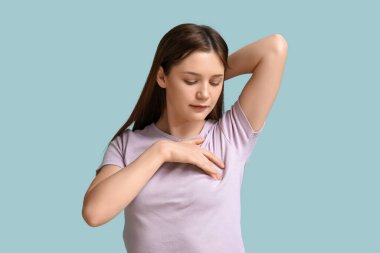 Mavi arka planda göğüslerini kontrol eden genç bir kadın.