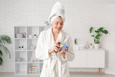 Evde duş aldıktan sonra saç derisi masaj aleti ve bir şişe kozmetik ürünü olan genç bir kadın.