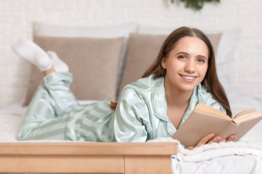 Genç mutlu kadın yatak odasında kitap okuyor.