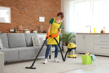 Evde elektrikli süpürge ve kulaklıkla halı temizleyen güzel bir kadın.