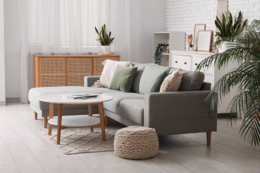 Beyaz tuğla duvarın yanında kanepesi, masası ve çekmeceleri olan bir oturma odası.