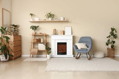 Şömineli oturma odası, raf ünitesi ve bej duvarın yanındaki gri sallanan sandalye.