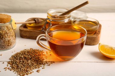 Limonlu bir bardak sıcak karabuğday çayı ve beyaz ahşap zemin üzerinde bal kaseleri.