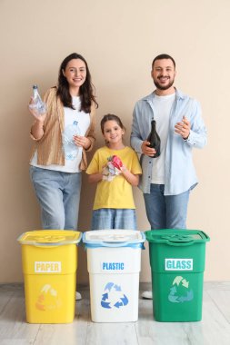 Bej duvarın yakınındaki çöpleri ayıran konteynırları olan bir aile. Küresel Geri Dönüşüm Günü