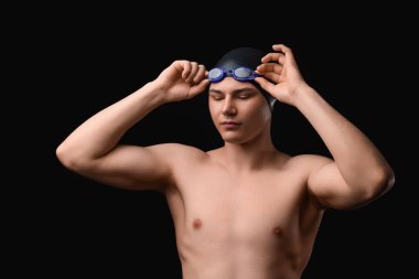 Erkek yüzücü koyu arkaplana karşı gözlük takıyor