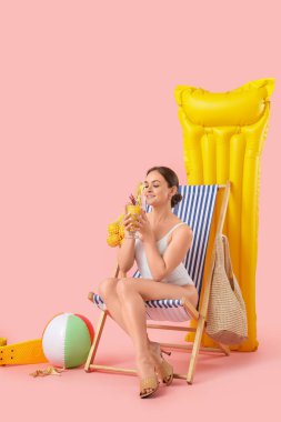 Güvertede oturan güzel bir kadın ve pembe arka planda plaj aksesuarları.