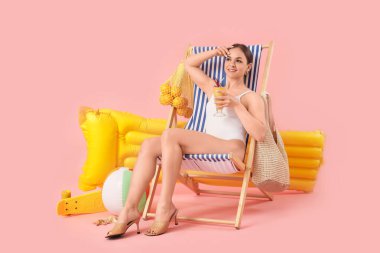 Güvertede oturan güzel bir kadın ve pembe arka planda plaj aksesuarları.