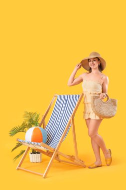 Sarı arka planda kumsal çantalı ve şezlonglu güzel kadın.