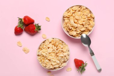 Lezzetli mısır gevreği ve pembe arka planda çilekli kaseler.