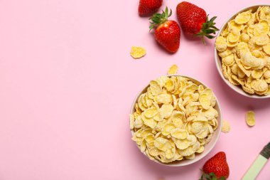 Lezzetli mısır gevreği ve pembe arka planda çilekli kaseler.