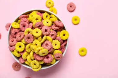 Pembe arka planda lezzetli mısır gevreği halkaları olan kase, yakın plan.