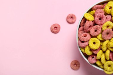 Pembe arka planda lezzetli mısır gevreği halkaları olan kase, yakın plan.