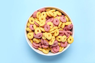 Mavi arka planda renk mısır gevreği halkaları olan kase, yakın plan.