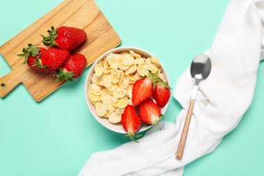 Turkuaz arka planda bir kase lezzetli mısır gevreği, çilek ve peçeteyle kompozisyon, yakın plan.