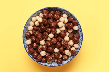 Sarı arka planda lezzetli çikolatalı mısır topları olan kase, yakın plan.