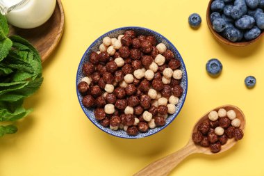 Bir kase lezzetli çikolatalı mısır topu, sarı arka planda kaşık ve böğürtlen, yakın plan.