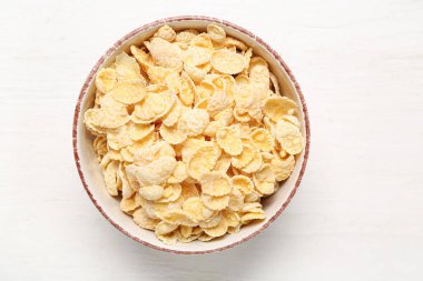 Beyaz ahşap arka planda lezzetli mısır gevrekleri olan kase, yakın plan.