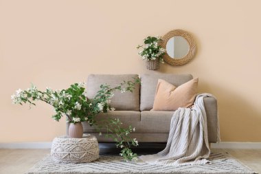 Rahat kanepe, puf ve çiçek açan yasemin çiçekleri oturma odasının iç tarafındaki bej duvarın yanında.