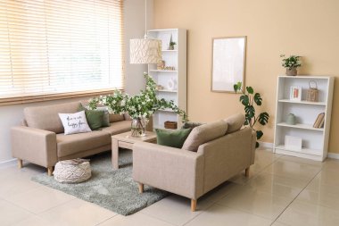 Konforlu kanepeler, masa ve vazo. Oturma odasının içinde çiçek açan yasemin çiçekleri.