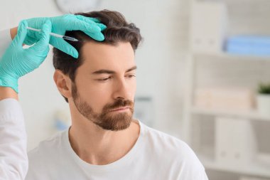 Doktor klinikte saç büyümesi için adama iğne yapıyor.