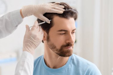 Doktor klinikte saç büyümesi için adama iğne yapıyor.