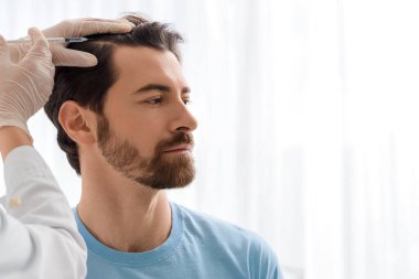 Doktor klinikte saç büyümesi için adama iğne yapıyor.