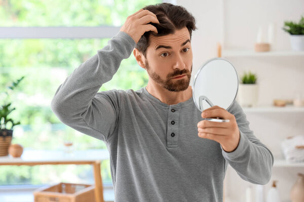 Человек с проблемой выпадения волос смотрит в зеркало
