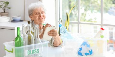 Mutfaktaki deftere çöp tenekeleri yazan son sınıf kadını. Atık sıralama kavramı