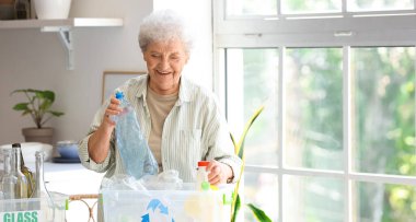 Mutfaktaki masasında çöp konteynırı olan yaşlı bir kadın. Atık sıralama kavramı